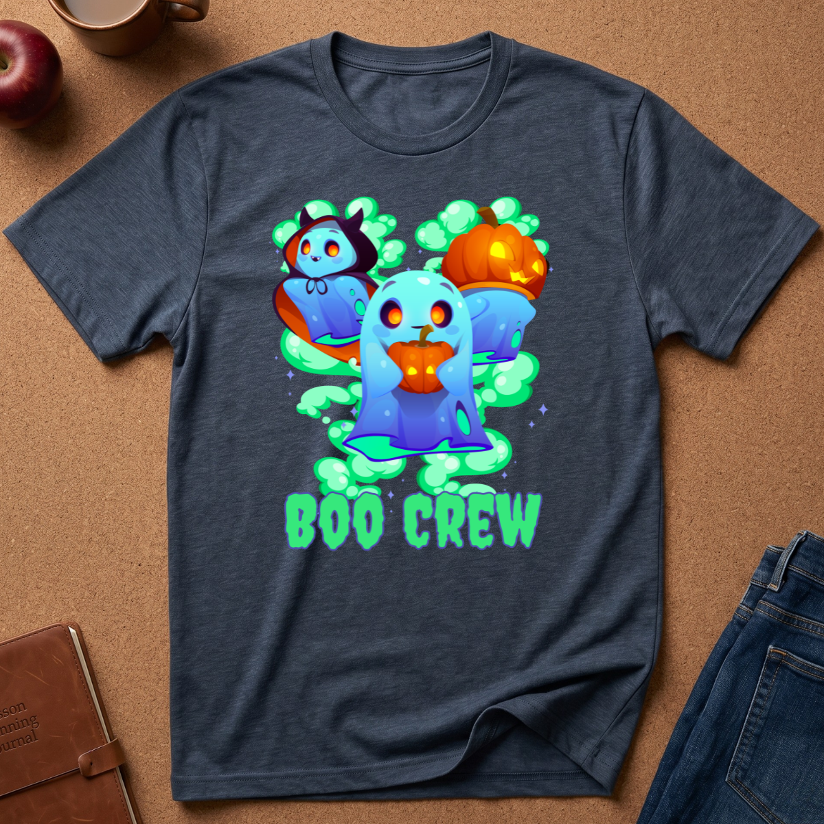 A dark heather gray graphic t-shirt laid flat on a brown cork background, featuring a colorful cartoon 'Boo Crew' design with ghosts, a vampire, a pumpkin, and green mist.