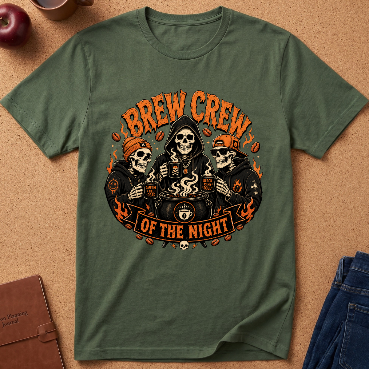 An olive green crewneck t-shirt with a 'Brew Crew of the Night' graphic print, laid flat on a cork background with lifestyle props like an apple, a notebook, and jeans.
