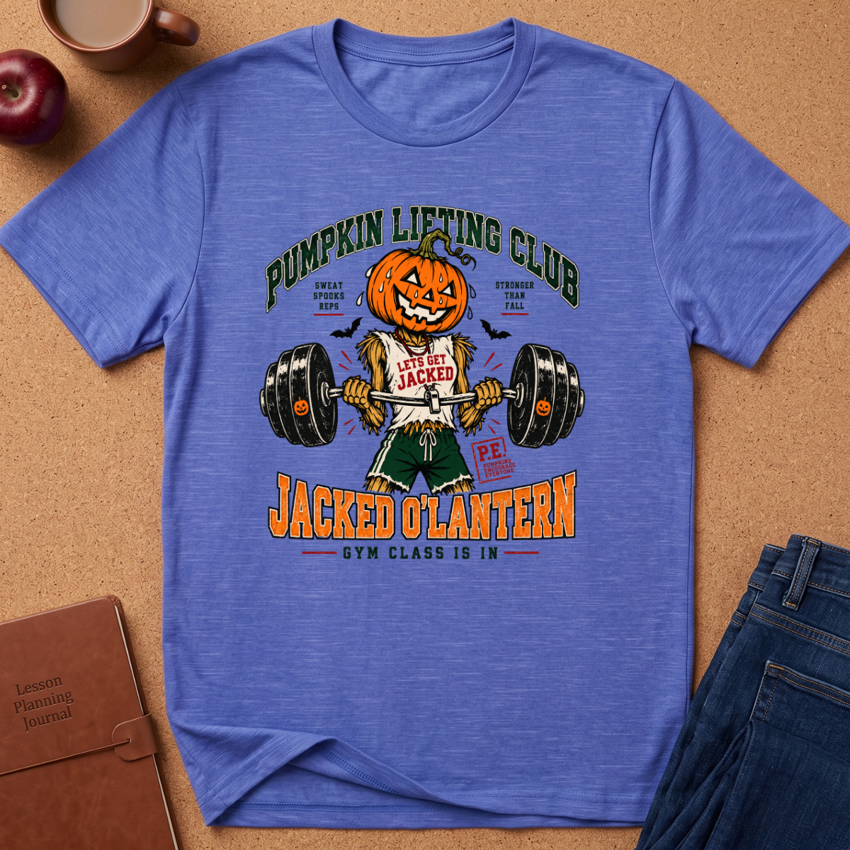 A heathered blue graphic t-shirt laid flat on a cork background, featuring a Halloween-themed design with a jack-o'-lantern lifting a barbell and the text 'Pumpkin Lifting Club' and 'Jacked O'Lantern'.