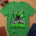 A green short-sleeve graphic T-shirt laid flat on a cork surface, featuring a wheelchair figure with raised arms and the words 'Cerebral Palsy STRONG' in white and green. A coffee mug, apple, notebook, and jeans are partially visible around it as styling props.