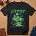 A Black graphic T-shirt with a UFO abducting a cow from a mountain valley, with a green li ht.  The text reads History is always watching.