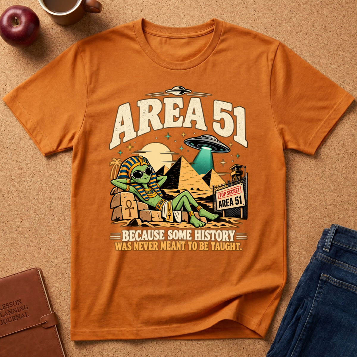 Orange  graphic t-shirt reads "area 51 because some History was never meant to be taught" With an alien wearing a pharoahs cloths, by the pyramids with a UFO