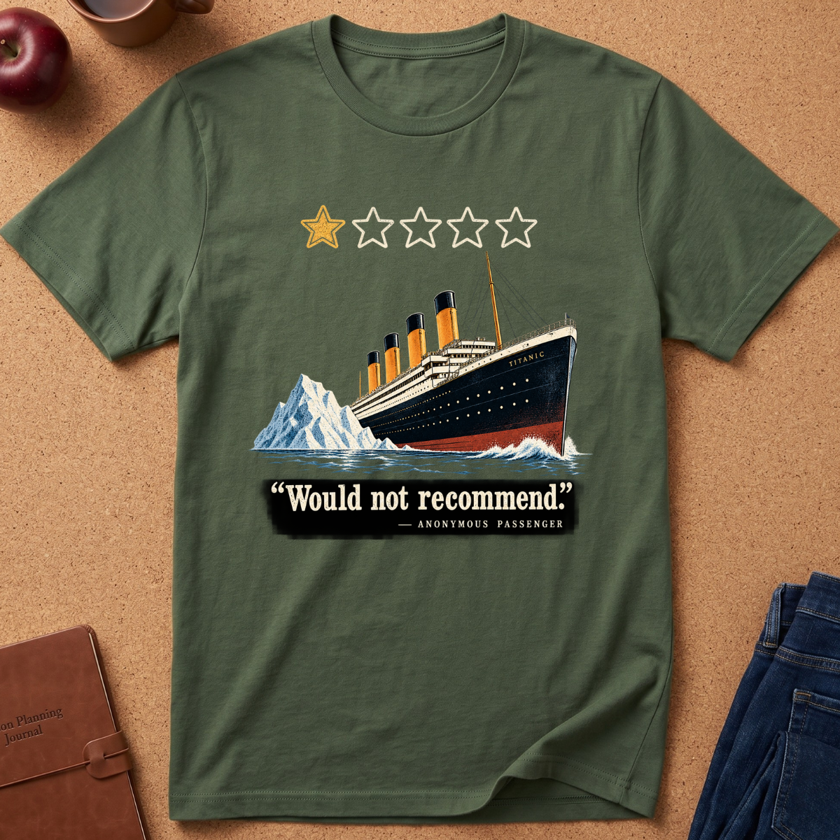 An olive green short-sleeve t-shirt laid flat on a cork background, featuring a Titanic-style illustration with a yellow star, four white stars, a black and cream ocean liner, icebergs, and the text “Would not recommend” with “Anonymous Passenger” underneath.
