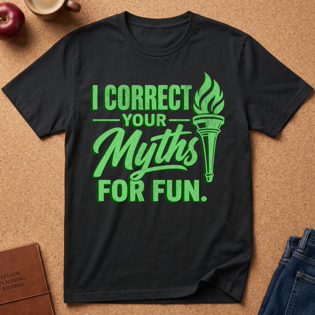 A black short-sleeve graphic T-shirt laid flat on a cork background, featuring bright green text that reads 'I CORRECT YOUR Myths FOR FUN.' with a torch illustration.