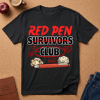 Black t-shirt with 'Red Pen Survivors Club' design on a brown surface with an apple, coffee, and jeans.