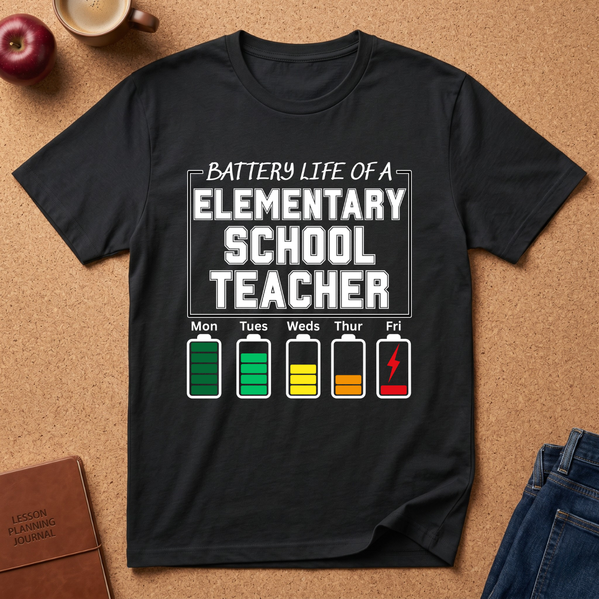 Black t-shirt with 'Battery Life of a Elementary School Teacher' graphic on a brown surface with school supplies.