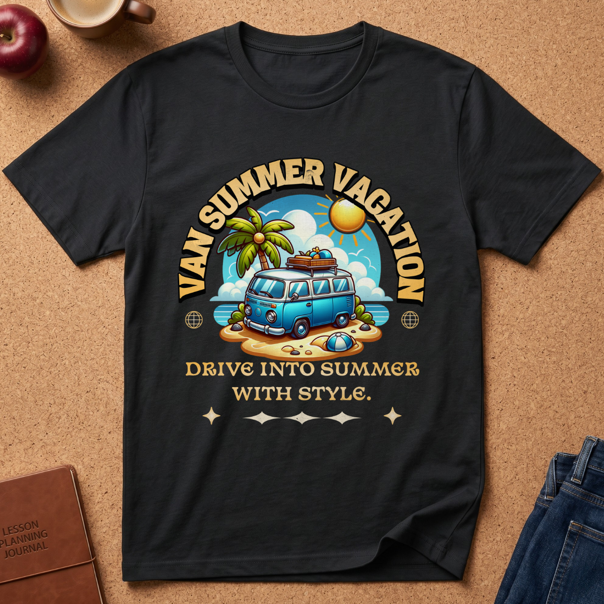 A black short-sleeve graphic T-shirt laid flat on a cork surface, featuring a retro-style beach scene with a blue van, palm tree, sun, and the text 'VAN SUMMER VACATION' and 'DRIVE INTO SUMMER WITH STYLE.' Styled props including an apple, coffee cup, notebook, and jeans are partially visible around the shirt.