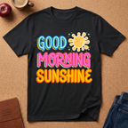 Black t-shirt with 'Good Morning Sunshine' text and sun graphic on a brown surface with accessories.