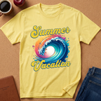 A yellow short-sleeve t-shirt laid flat on a cork-like surface, featuring a colorful graphic of a wave with the words 'Summer Vacation' in yellow script. Surrounding props include a coffee cup, an apple, a notebook, and folded blue jeans.