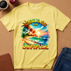A yellow short-sleeve t-shirt with a colorful graphic print reading 'SCHOOL'S OUT FOR SUMMER' over a tropical beach scene, laid flat on a cork surface with jeans, a coffee mug, and a notebook nearby.