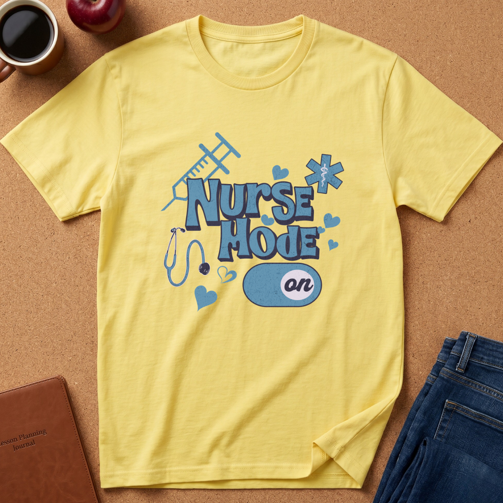 A yellow short-sleeve crewneck t-shirt with a blue 'Nurse Mode On' graphic, laid flat on a cork background with lifestyle props including a coffee mug, apple, notebook, and jeans.