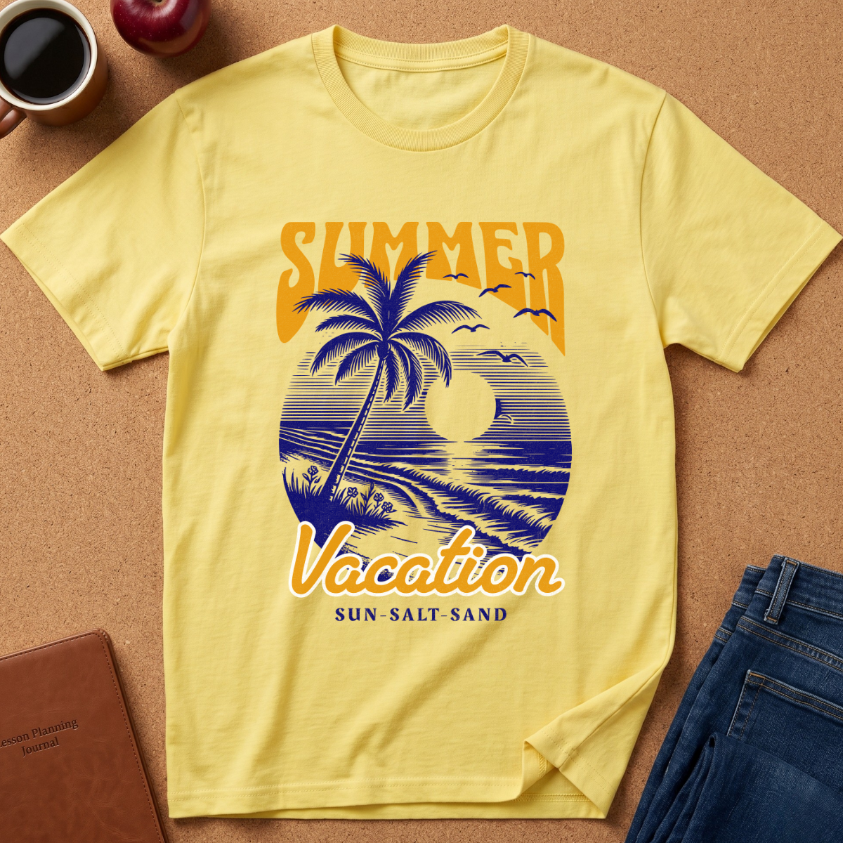 A pale yellow short-sleeve T-shirt laid flat on a cork-like surface, featuring a retro beach sunset graphic with a palm tree, blue waves, birds, and the words “SUMMER Vacation” and “SUN-SALT SAND.” Coffee cup, apple, notebook, and jeans are placed around it as styling props.