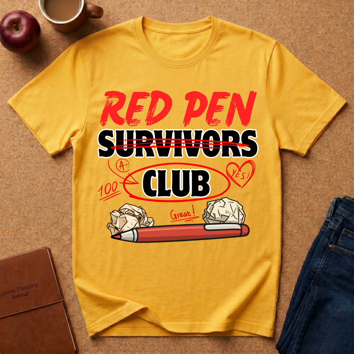 Yellow t-shirt with 'Red Pen Survivors Club' design on a brown surface with an apple, coffee cup, and jeans.