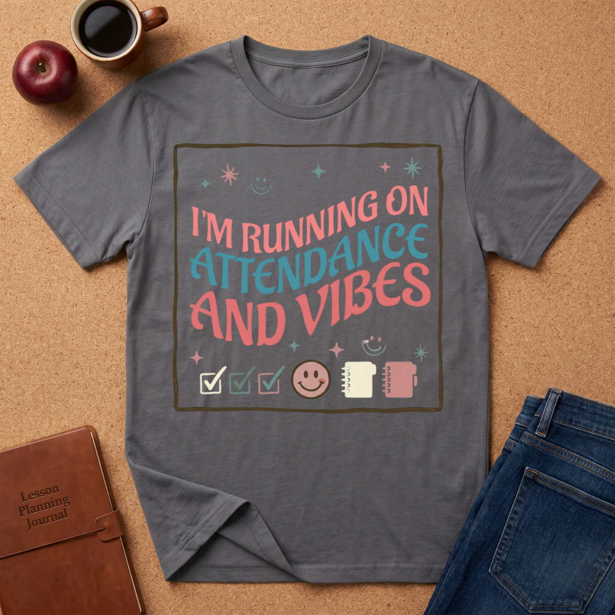 Gray t-shirt with 'I'm Running on Attendance and Vibes' text on a brown surface with an apple, coffee cup, and jeans.
