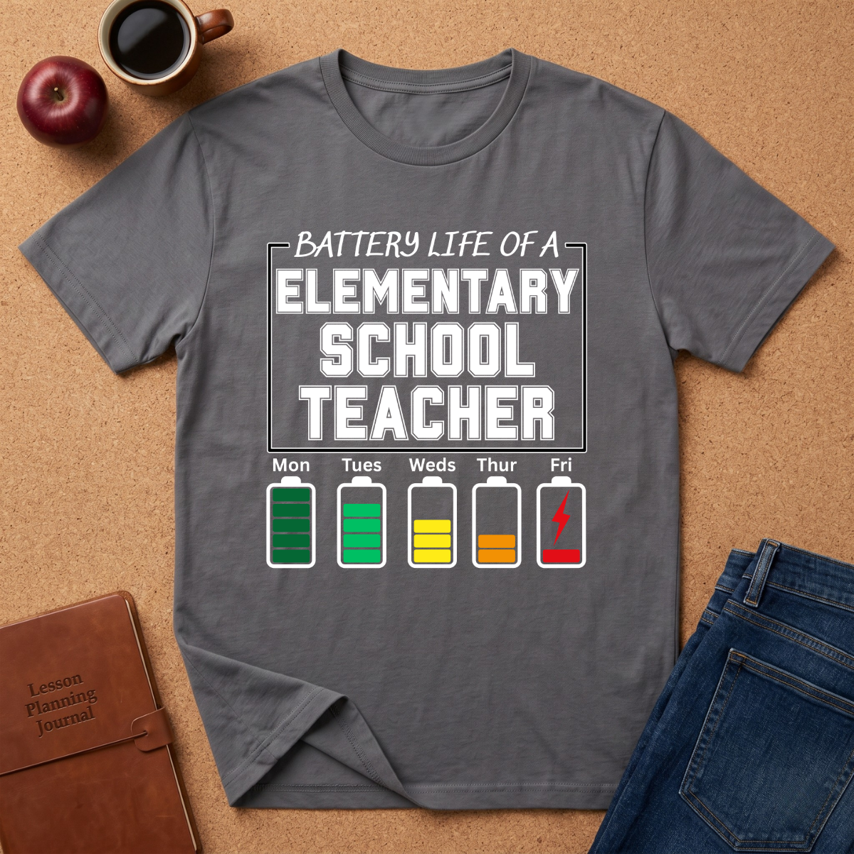 Gray t-shirt with 'Battery Life of a Elementary School Teacher' graphic on a brown surface with a coffee cup, apple, and notebook.