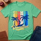 A green heather short-sleeve t-shirt laid flat on a cork background, featuring a retro-style 'Summer Vacation' graphic with colorful vertical stripes, palm trees, and a silhouette of a person in a boat. Styled flat-lay props include an apple, a coffee cup, a brown journal, and blue jeans.