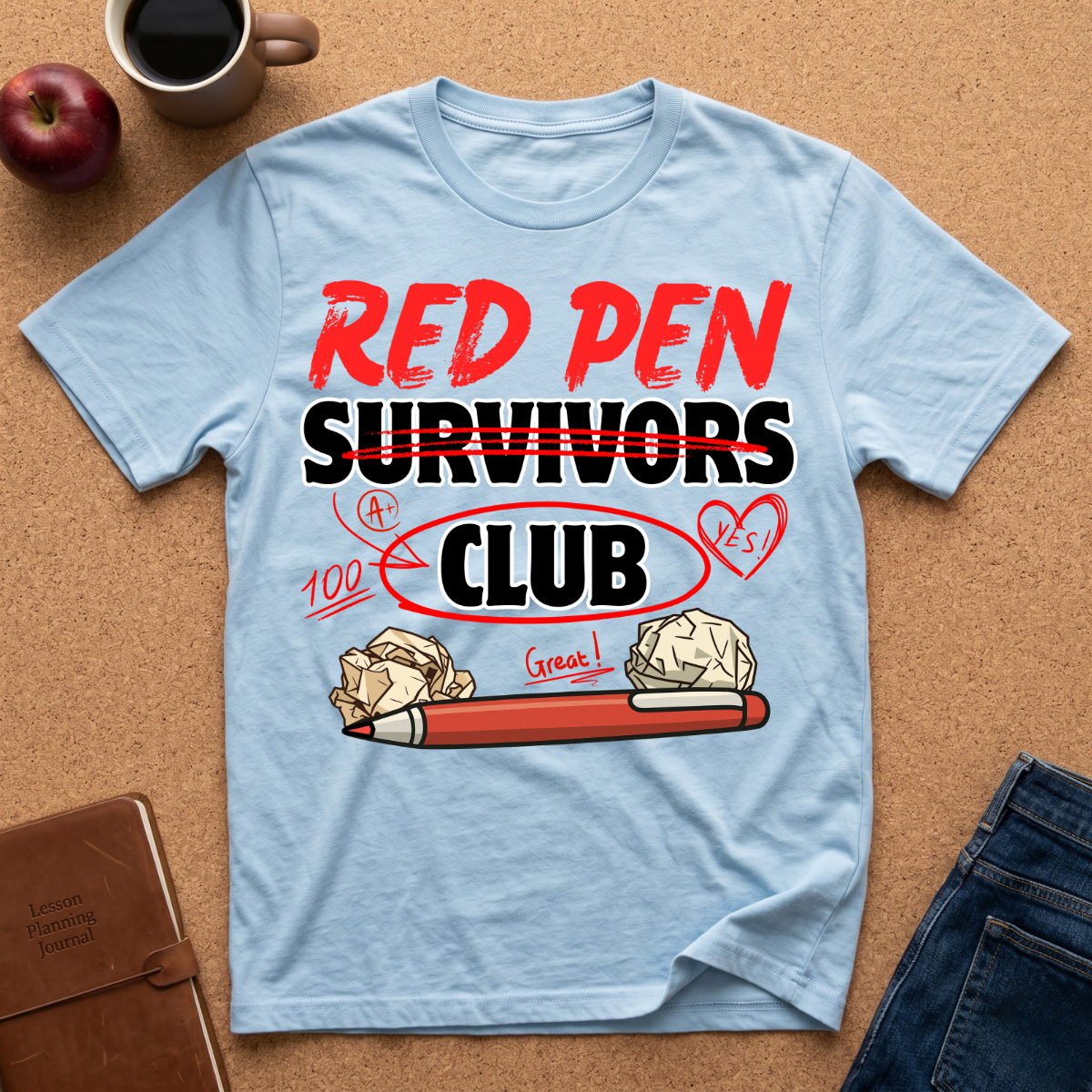 Light blue t-shirt with 'Red Pen Survivors Club' design on a brown surface with an apple, coffee, and jeans.