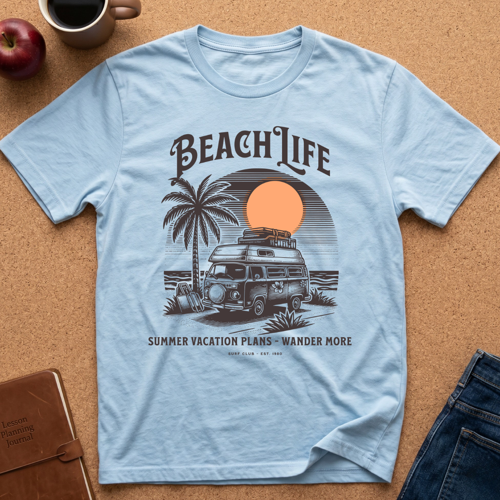 A light blue graphic t-shirt laid flat on a cork background, featuring a retro-style illustration of a camper van, palm tree, and sunset with the text 'BEACH LIFE' and 'SUMMER VACATION PLANS - WANDER MORE'. A red apple, coffee mug, notebook, and jeans are styled around it.