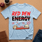 Light blue t-shirt with 'Red Pen Energy' and positive marks graphic on a brown surface with an apple, coffee, and jeans.