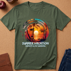 An olive green short-sleeve t-shirt laid flat on a cork background, featuring a colorful retro sunset graphic with palm trees and the text 'SUMMER VACATION SUNSETS & NO GRADING'.
