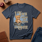 A navy blue graphic t-shirt laid flat on a brown cork background, featuring a teddy bear sitting on books with the text 'I TEACH INSPIRE AND SURVIVE ON COFFEE'. A red apple, a coffee mug, a notebook, and blue jeans are styled around the shirt.
