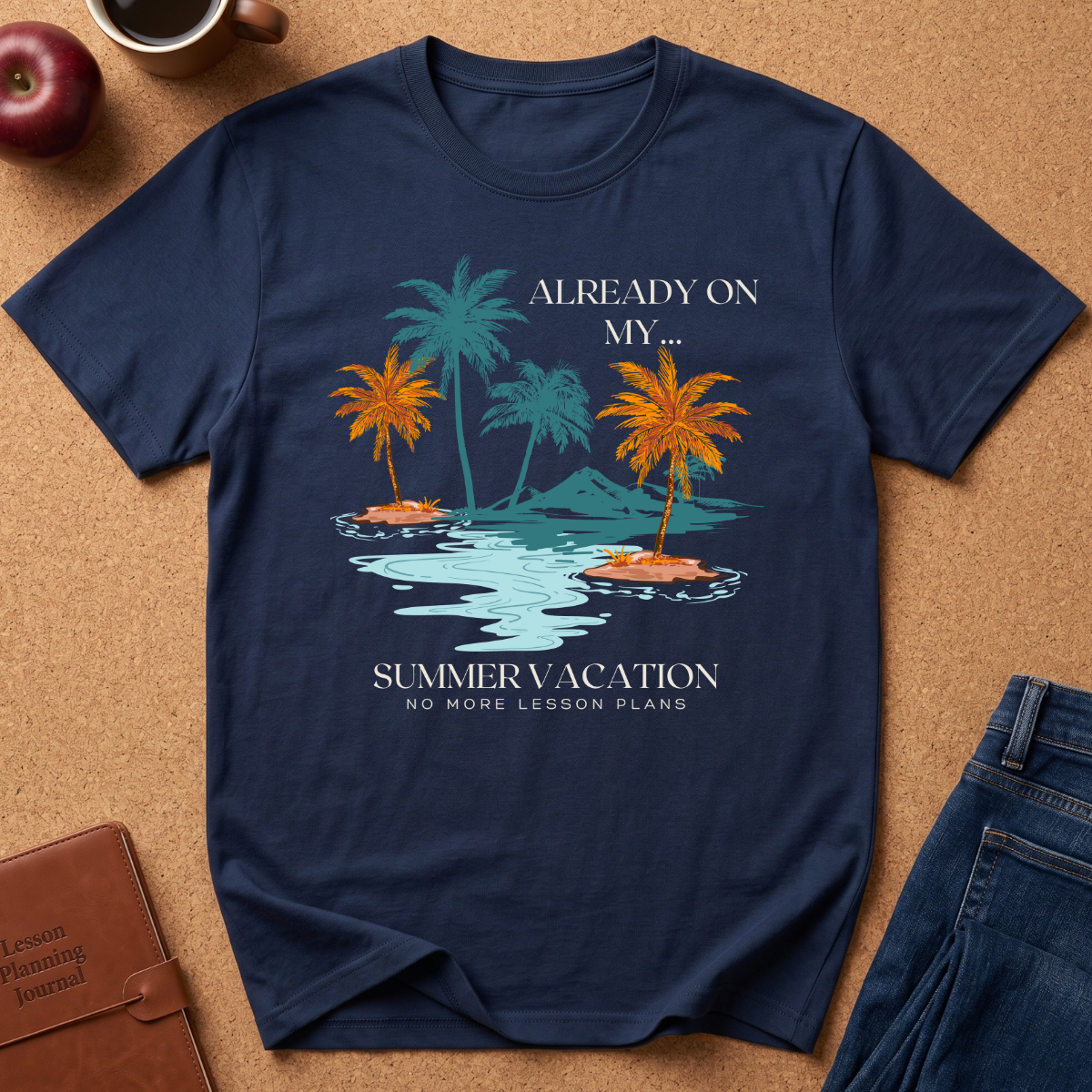A navy blue graphic t-shirt laid flat on a cork background, featuring a tropical island design with palm trees, water, and the text 'ALREADY ON MY SUMMER VACATION, No More Lesson Plans.