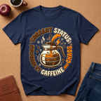 Navy blue graphic t-shirt says "Current Status, Powered by Caffeine and Chaos" with coffee-themed graphic and text on a brown surface with accessories.