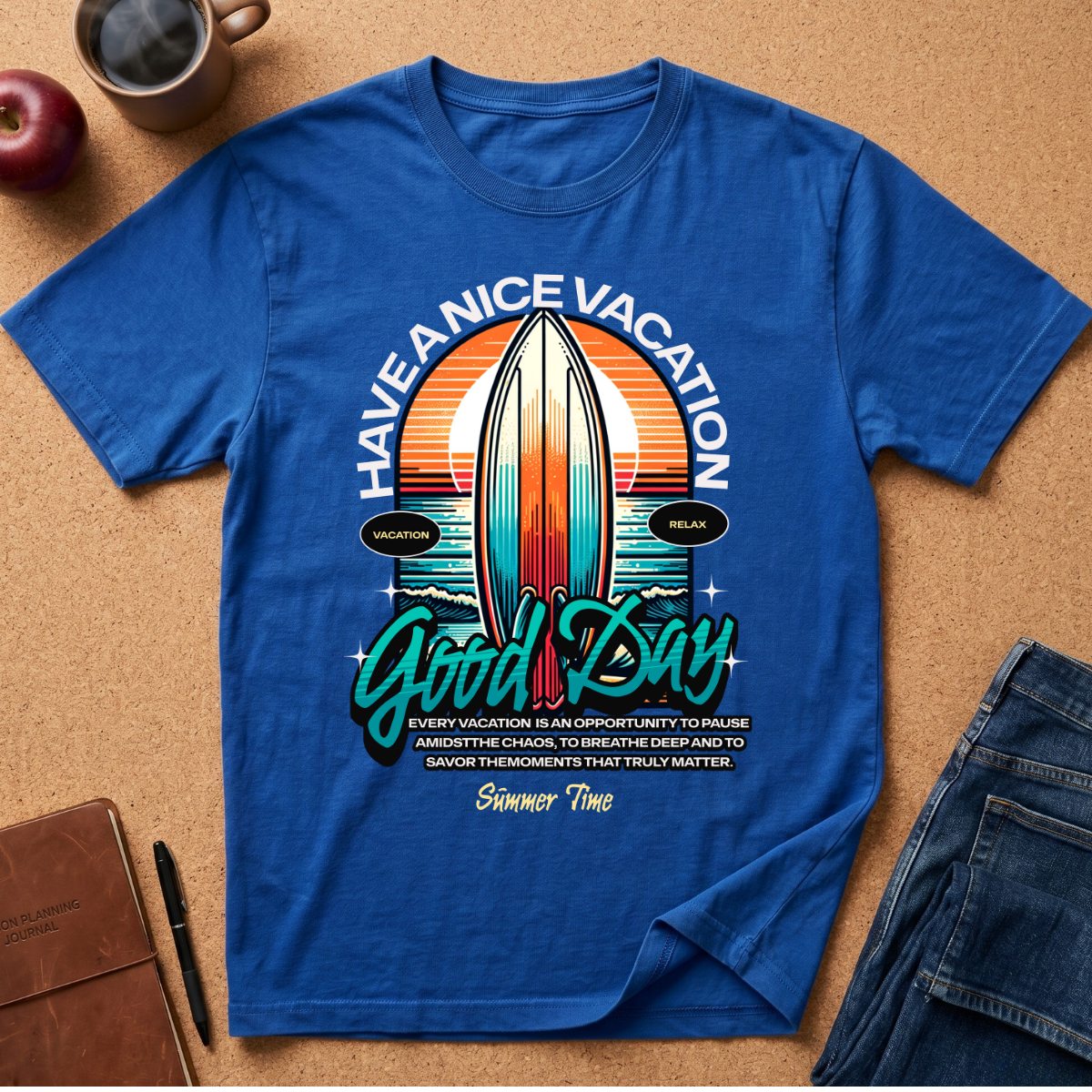 A royal blue short-sleeve graphic T-shirt laid flat on a cork surface, surrounded by lifestyle props including a coffee mug, apple, notebook, pen, and jeans. The shirt features a retro surfboard sunset graphic with the text 'HAVE A NICE VACATION Good Day' and smaller slogan text below.