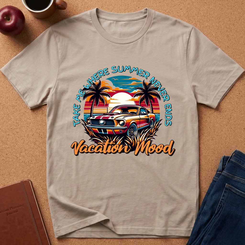 A beige graphic t-shirt laid flat on a cork background, featuring a retro-style illustration of a classic car at sunset with palm trees and the text 'TAKE ME HERE SUMMER VACATION MOOD' and 'Vacation Mood'. Props like an apple, coffee cup, notebook, and jeans are visible around the shirt.