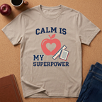 Beige t-shirt with 'Calm is my superpower' design featuring an apple and notebook on a brown surface.