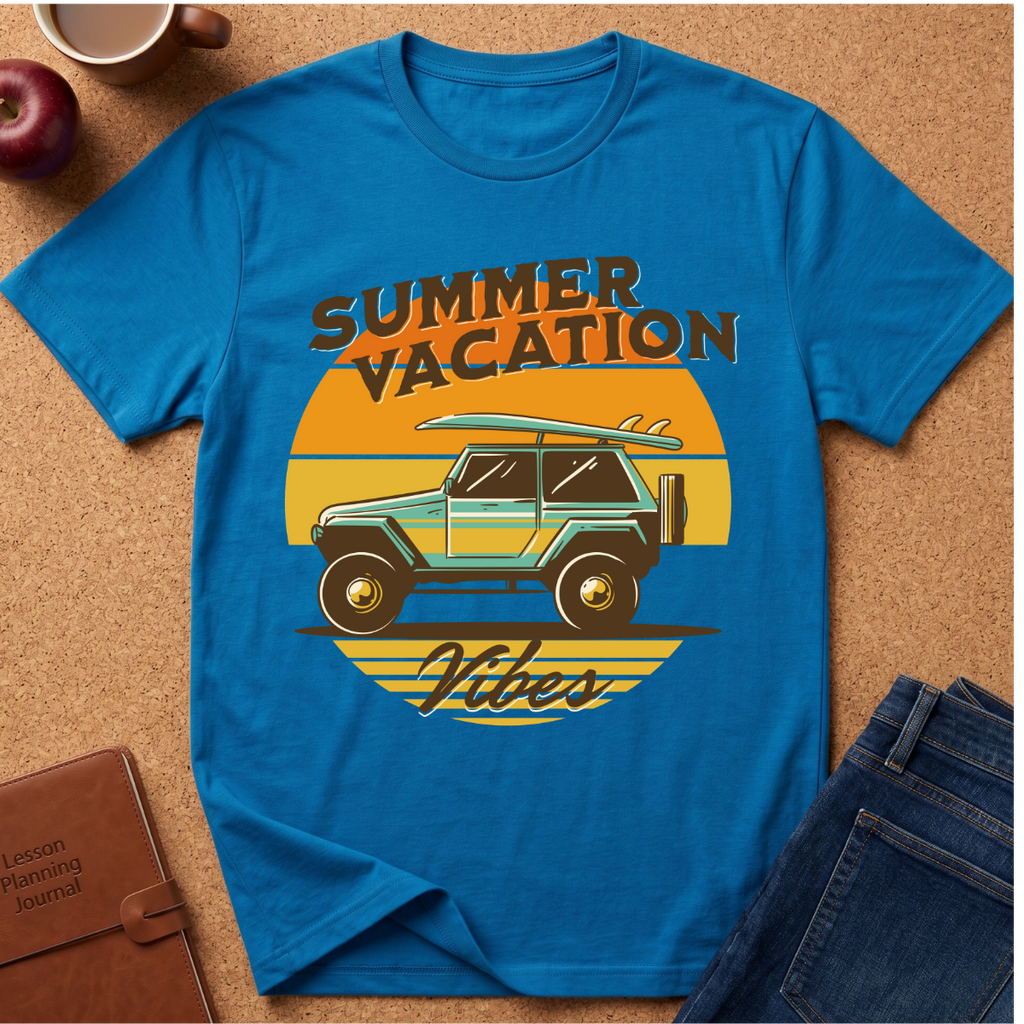 A bright blue graphic t-shirt laid flat on a cork surface, featuring a retro sunset design with a teal jeep, surfboard, and the words 'SUMMER VACATION Vibes.' Surrounding props include jeans, an apple, a coffee cup, and a journal.