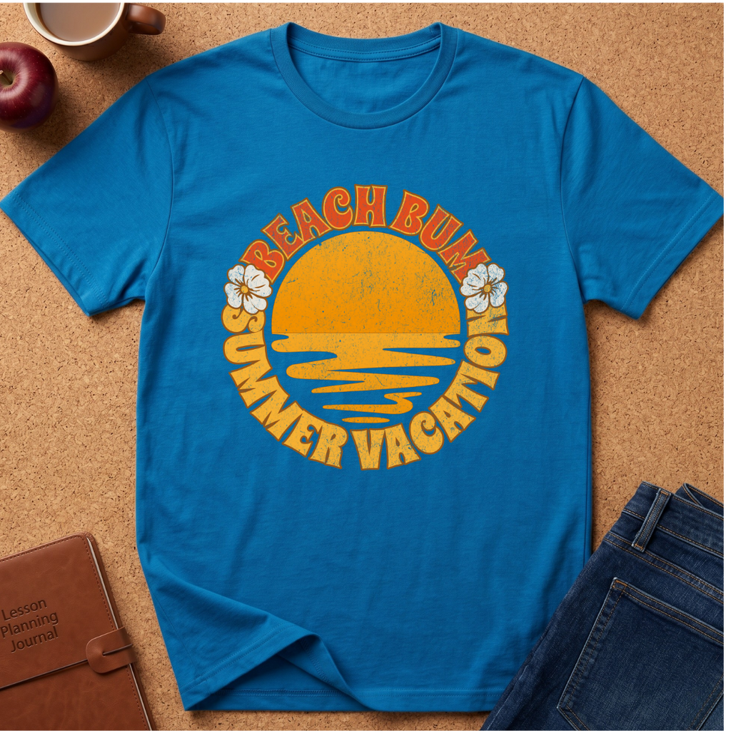 Saphire short-sleeve t-shirt laid flat on a cork background, featuring a retro-style yellow and orange graphic with the words 'BEACH BUM SUMMER VACATION' and small white flower illustrations.