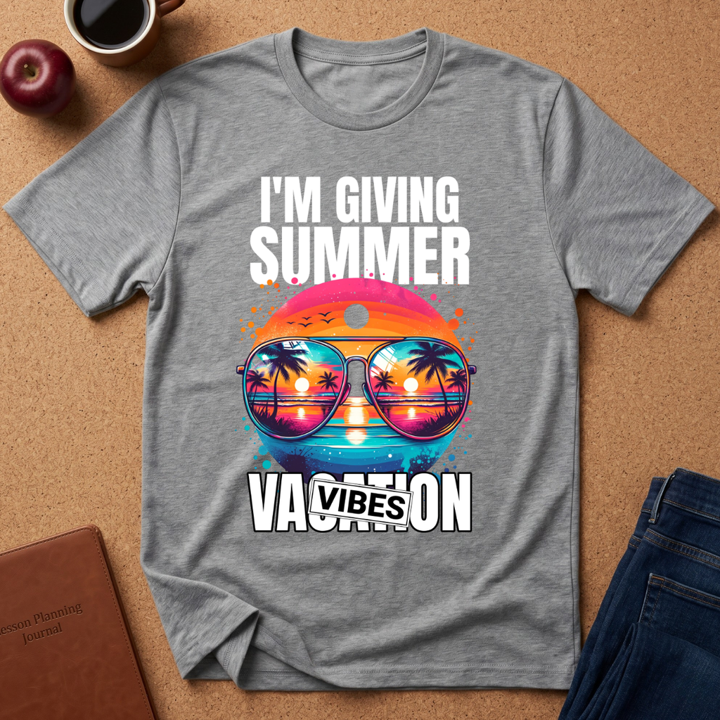 A heather gray graphic t-shirt laid flat on a cork background, featuring a colorful retro design with sunglasses reflecting a sunset beach scene and the text 'I'M GIVING SUMMER VACATION VIBES'.