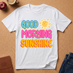 White t-shirt with 'Good Morning Sunshine' text on a brown surface with an apple, coffee cup, and jeans.
