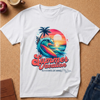 A white short-sleeve T-shirt laid flat on a cork surface, featuring a colorful retro-style summer vacation graphic with a wave, palm tree, sunset, and the text 'Summer Vacation IS A STATE OF MIND.' Partial props around the shirt include a cup, apple, notebook, and jeans.