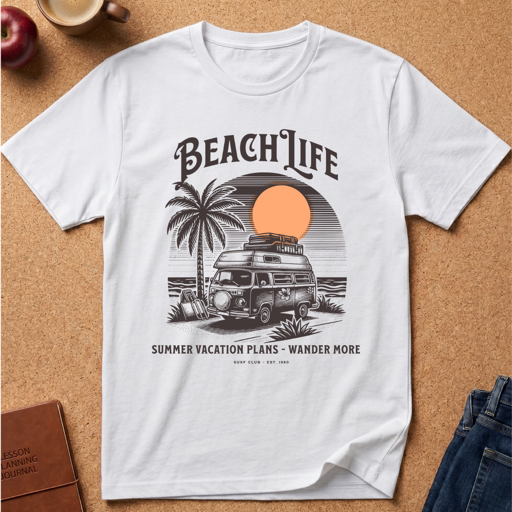 A white short-sleeve graphic T-shirt laid flat on a cork surface, featuring a retro beach-themed print with the words “BEACH LIFE,” a palm tree, a vintage camper van, a sunset circle, and smaller text reading “SUMMER VACATION PLANS - WANDER MORE.” Partial props including an apple, a coffee cup, a book, and jeans are visible around the shirt.