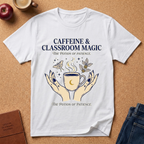 White t-shirt with 'Caffeine & Classroom Magic' design on a brown surface with a coffee cup, apple, and jeans.