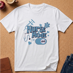 A white short-sleeve crewneck t-shirt with a 'Nurse Mode On' graphic in shades of blue, laid flat on a cork board background with lifestyle props like an apple, a coffee mug, and jeans.