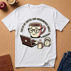 White Graphic t-shirt says 'Fueled by coffee an unanswered emails', with a coffee-themed graphic on a brown surface with accessories.