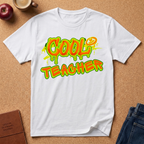 White t-shirt with 'COOL TEACHER' text on a brown surface with educational items.