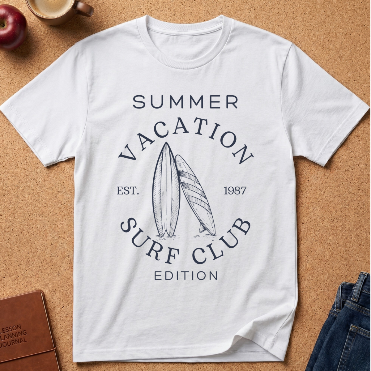 A white short-sleeve T-shirt laid flat on a cork surface, featuring a navy graphic that reads “SUMMER VACATION SURF CLUB EST. 1987 EDITION” with two surfboards in the center.