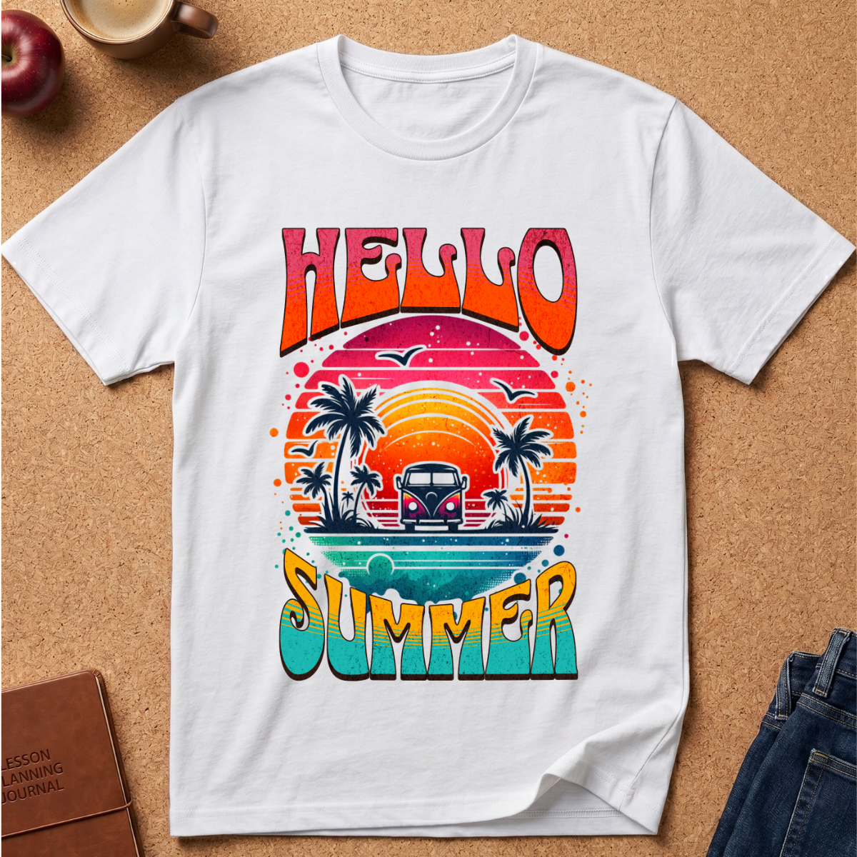 A white short-sleeve T-shirt laid flat on a cork surface, featuring a colorful retro-style graphic with the words “HELLO SUMMER” and a sunset scene with palm trees, birds, and a van.