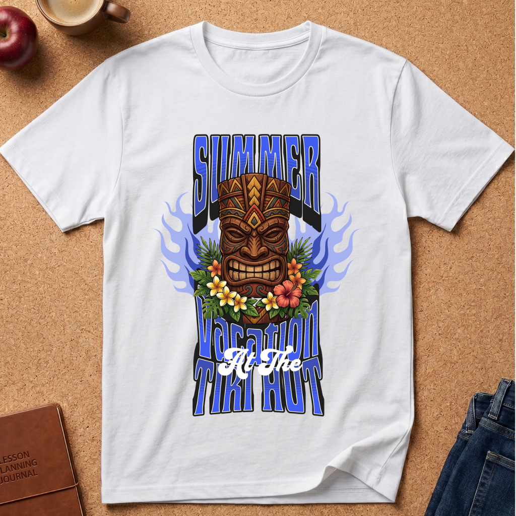 A white short-sleeve graphic T-shirt laid flat on a cork background, featuring a large tiki mask design with blue flame-like side elements, flowers across the chest, and stylized text reading 'SUMMER TUITI HOUR' plus 'All The'.