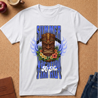A white short-sleeve graphic T-shirt laid flat on a cork background, featuring a large tiki mask design with blue flame-like side elements, flowers across the chest, and stylized text reading 'SUMMER TUITI HOUR' plus 'All The'.